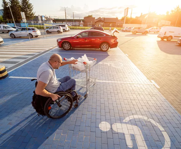 Mężczyzna na wózku podjeżdża z zakupami do miejsca parkingowego dla niepełnosprawnych. Kto może parkować na miejscu dla inwalidów?