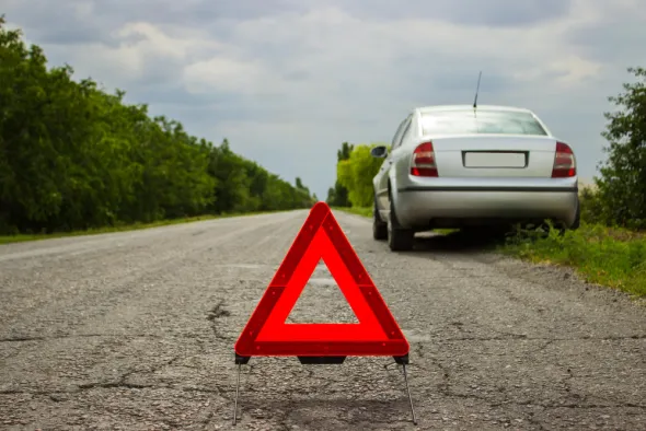Uszkodzone w kolizji auto stoi na poboczu, czekając na pomoc drogową. na pierwszym planie trójkąt bezpieczeństwa