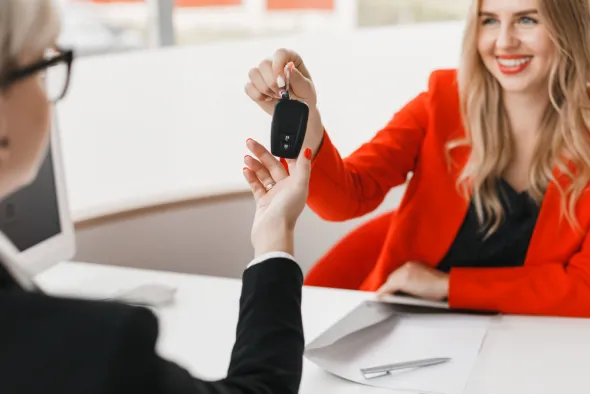 Młoda zadowolona kobieta przekazuje kluczyki od auta po zakończonym najmie długoterminowym