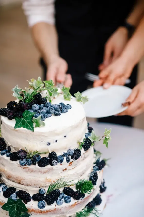 Bride and groom celebrating wedding cake tradition with blueberries