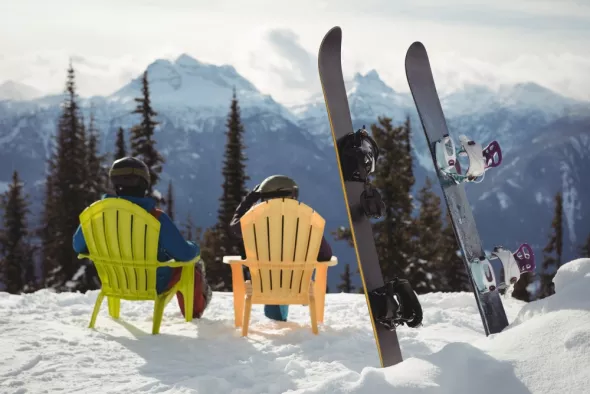 Couple sitting chair by snowboards snow covered mountain