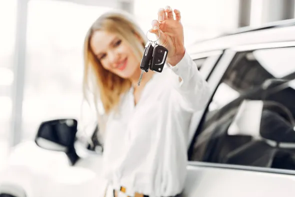 A young blonde woman stands next to a sleek rental car, ready to set off on a journey.