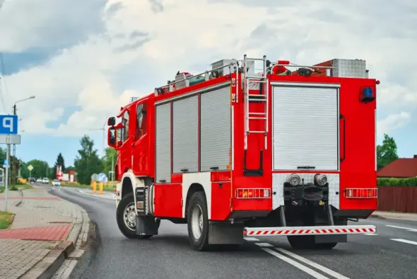 A fire engine driving along a suburban street in Poland on a cloudy day, illustrating situations where drivers must give way and exercise caution on the road