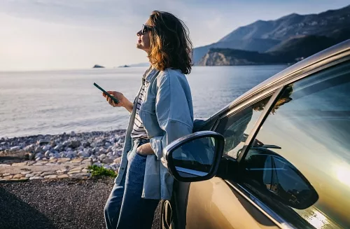 A girl resting by the sea, leaning against a car