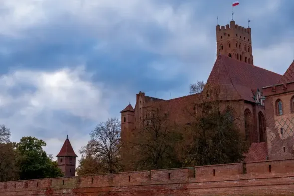 Red brick walls and keep of Malbork Castle surrounded by autumn trees in Poland