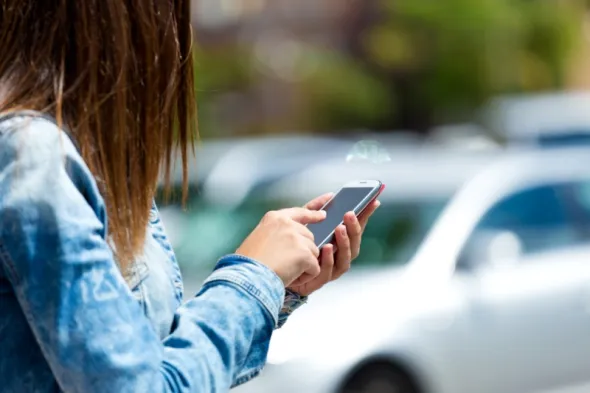 Młoda kobieta płaci telefonem poprzez aplikację mobilną za parkowanie w strefie płatnego parkowania