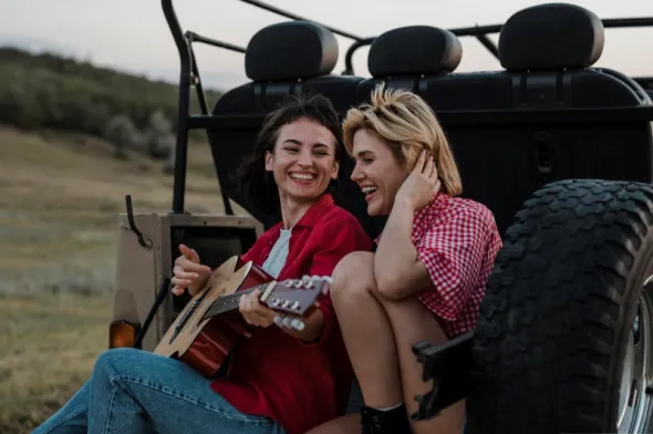 Roześmiane dziewczyny grają na gitarze podczas przerwy w samochodowej przejażdżce po bezdrożach