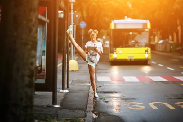 Kobieta stojąca na przystanku tuż przy buspasie, którym zbliża się żółty autobus