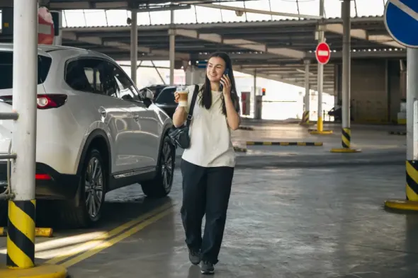 Young woman talking on the phone while holding coffee in a parking lot near Kraków Airport Balice.