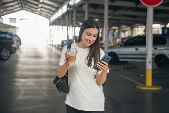 A woman with a cup of coffee in the parking lot at Gdańsk Airport before her trip.