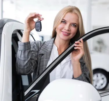 Młoda kobieta cieszy się odbierając nowy biały pojazd z wypożyczalni samochodów 