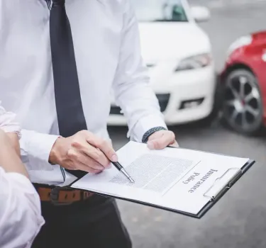 Mężczyzna wypisujący polisę OC samochodową na tle dwóch aut stojących na drodze