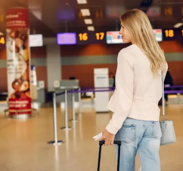 Beautiful young woman standing at airport terminal with luggage
