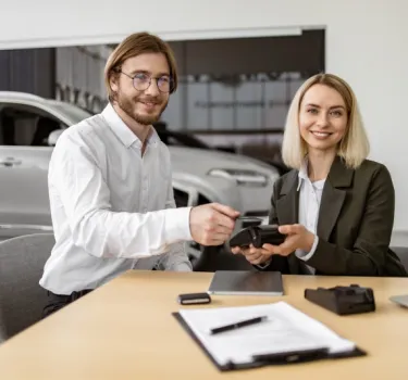 A woman watches as a man makes a card payment on a terminal while renting a car.