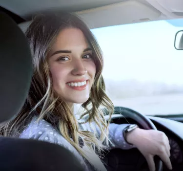 A smiling woman driving a Kaizen Rent car
