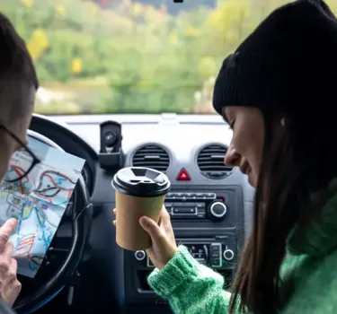 A couple of tourists sitting in a car in Poland, looking at a paper map and planning their route with Kaizen Rent 