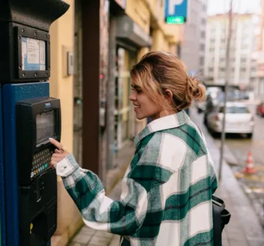 Młoda kobieta w koszuli w kratę płaci za parking przy parkomacie - Strefa Płatnego Parkowania w Krakowie