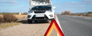 Uszkodzony biały  samochód na poboczu, zabezpieczony trójkątem. Kolizja drogowa wypożyczonym samochodem