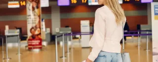 Beautiful young woman standing at airport terminal with luggage