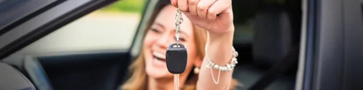 Radosna młoda kobieta z kluczykami w dłoni siedzi za kierownicą samochodu