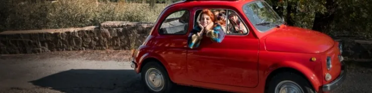 Mały czerwony samochód  jadący drogą w otoczeniu oliwnych gajów 