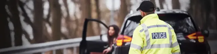 Policjant zmierza w kierunku zatrzymanego samochodu. Nowy taryfikator mandatów 2026