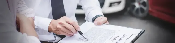 Mężczyzna wypisujący polisę OC samochodową na tle dwóch aut stojących na drodze