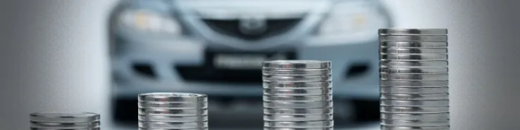 Wieża z monet  na tle rozmytego samochodu, symbolizująca rozliczenie VAT za wynajem długoterminowy samochodu
