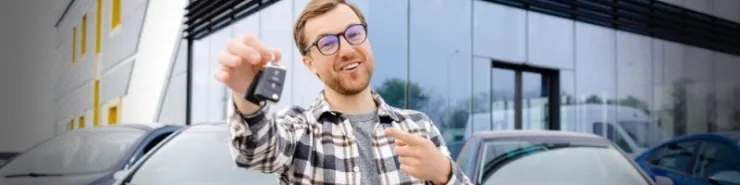 Zadowolony mężczyzna z kluczykami w dłoni stojący na parkingu wypożyczalni samochodów