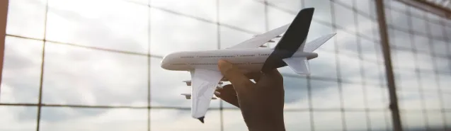 Hand holding a model aeroplane in front of an airport window