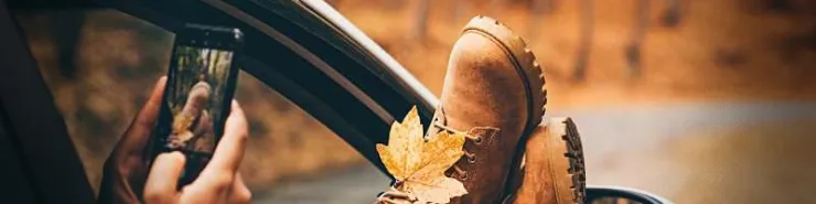 A car set against an autumn backdrop. A passenger relaxes with their phone, legs stretched out of the window. A close-up of shoes, with a falling leaf resting on them
