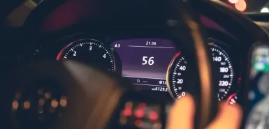 A woman is driving at night, holding the steering wheel, with the speedometer visible on the screen – an illustration relating to speed limits in Poland.