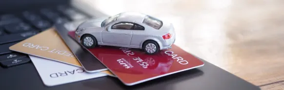 A small model car lying on a pile of payment cards, symbolising car rental without a credit card.